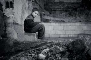 石壁の前でうつむいて座る人のモノクロ写真