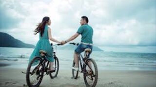 海辺の道を自転車で並んで走るカップル
