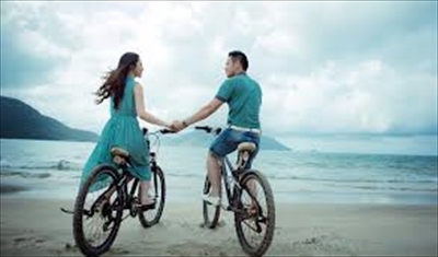 海辺の道を自転車で並んで走るカップル