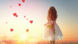 夕日に向かって立つ女性と舞う赤いハート