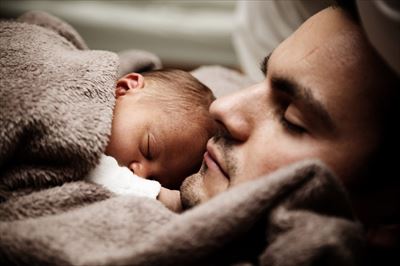 眠る赤ちゃんに頬を寄せる父親